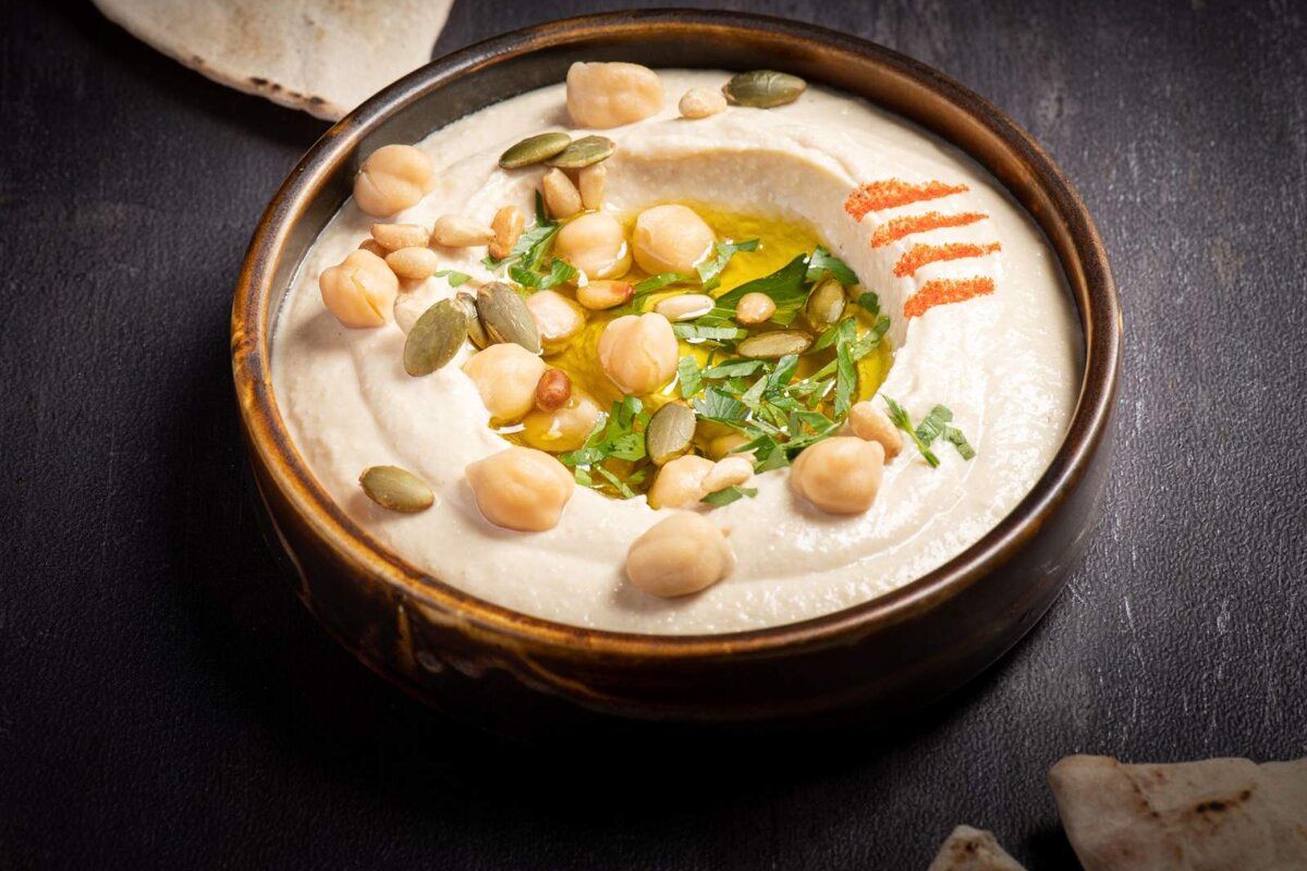 A bowl of hummus with chickpeas and pumpkin seeds