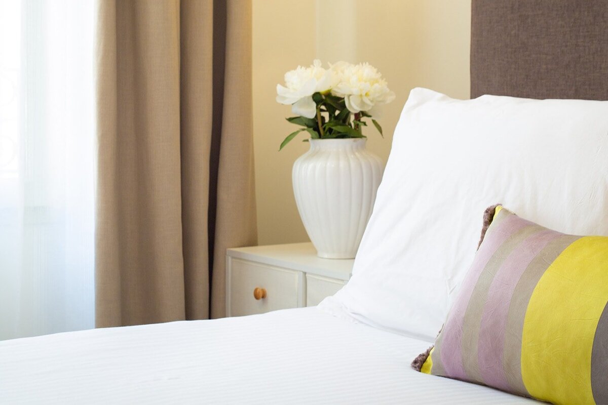 A vase of flowers sits on a nightstand next to a bed