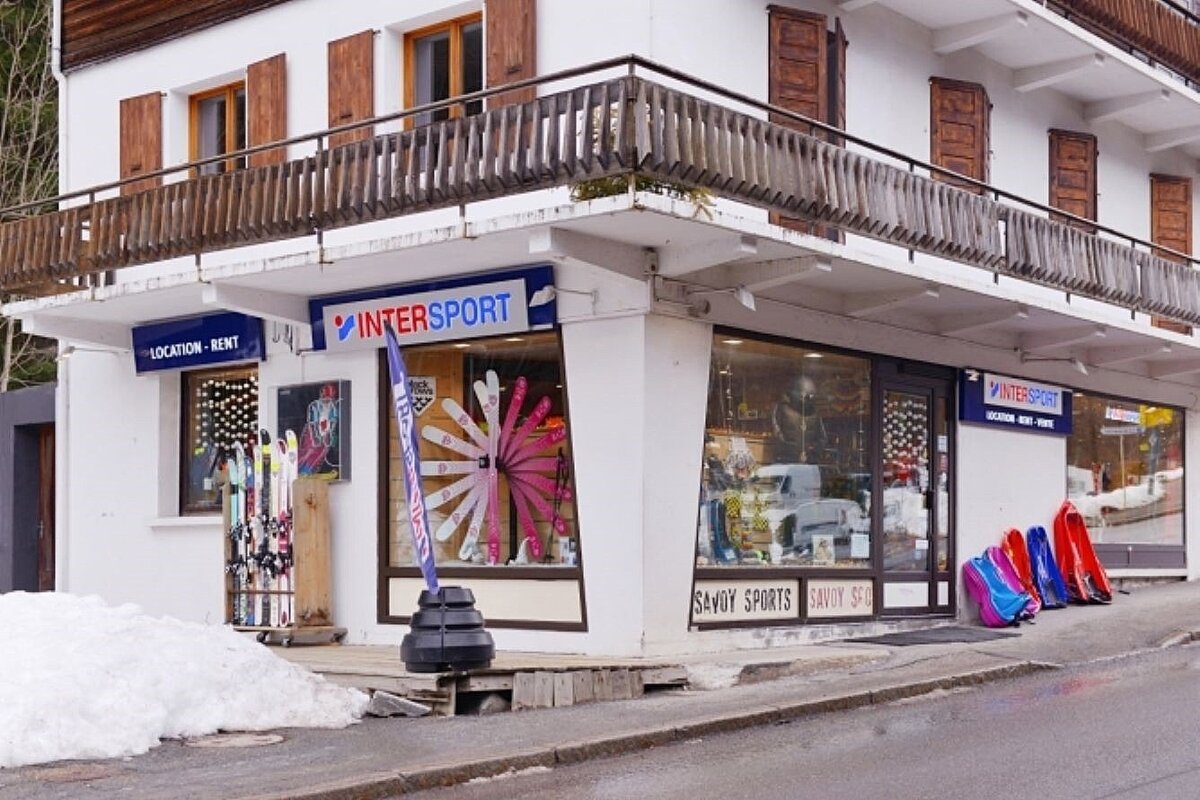 An Intersport ski rental shop featuring skis, sleds, and snow outside a building with wooden balconies.
