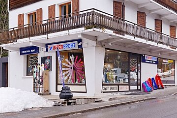 An Intersport ski rental shop featuring skis, sleds, and snow outside a building with wooden balconies.