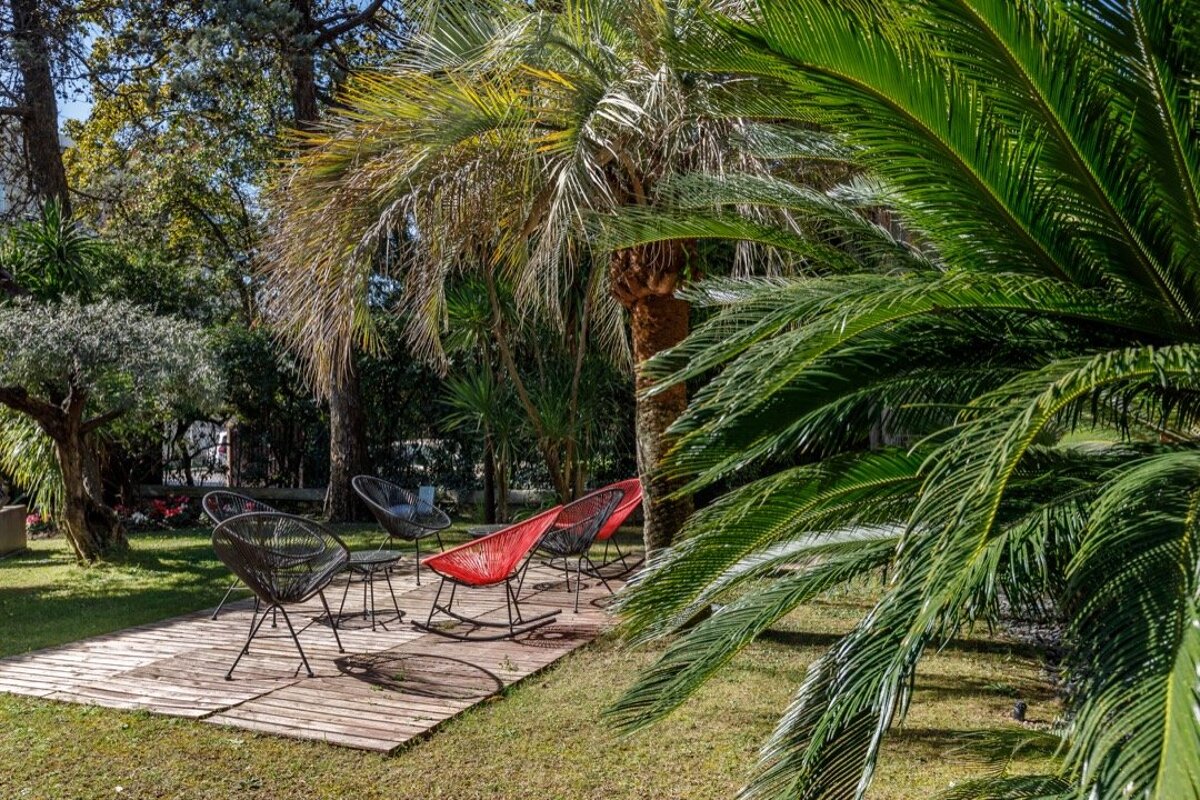 A row of rocking chairs in a garden surrounded by palm trees