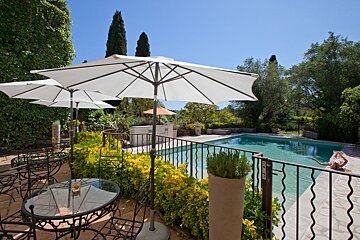 A swimming pool with a table and chairs under umbrellas