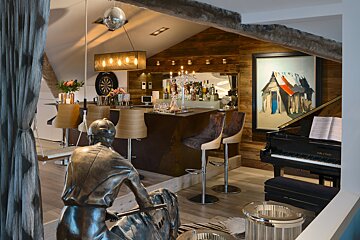 A statue of a man sits in a room with a piano and a dart board
