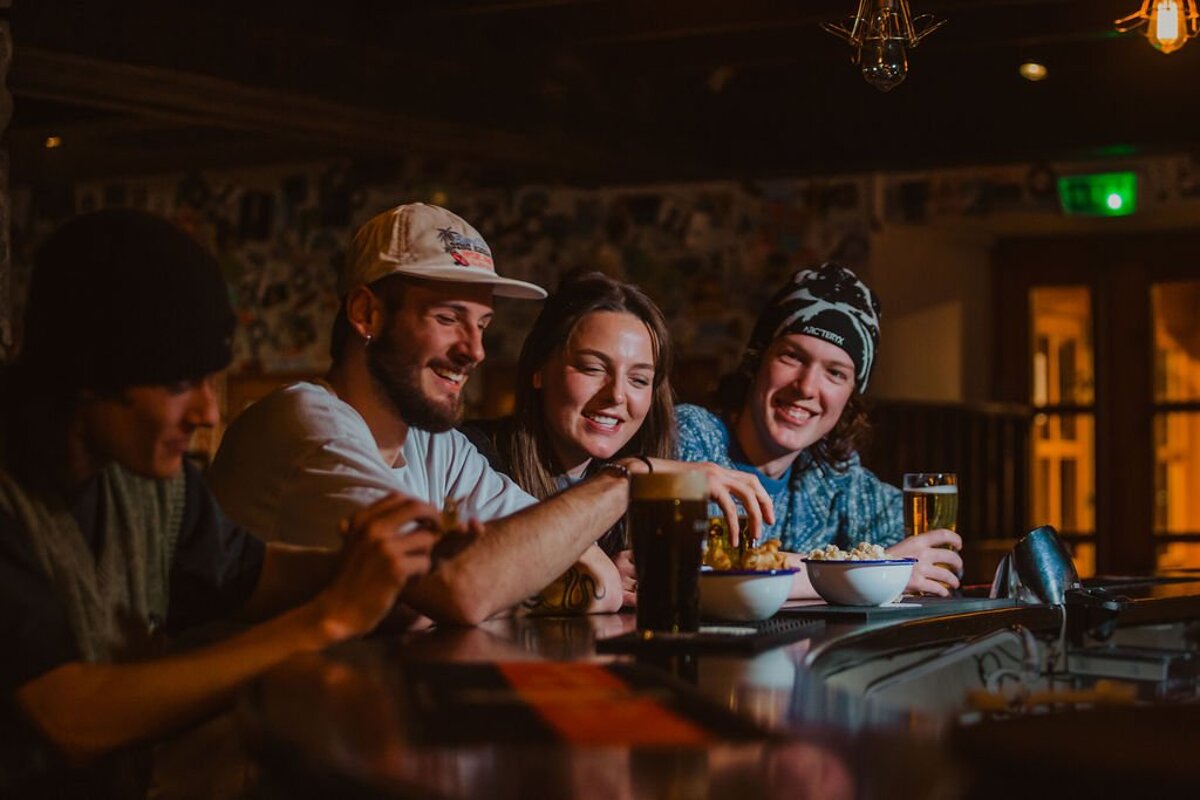 A group of people sitting at a bar with one wearing a hat that says red bull