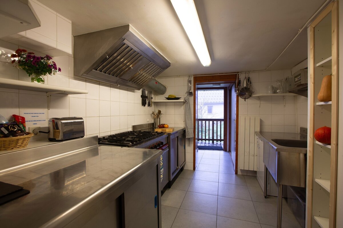 A bright, industrial-style kitchen features stainless steel counters, a large stove, and white tiled walls. A doorway leads to an outdoor balcony.