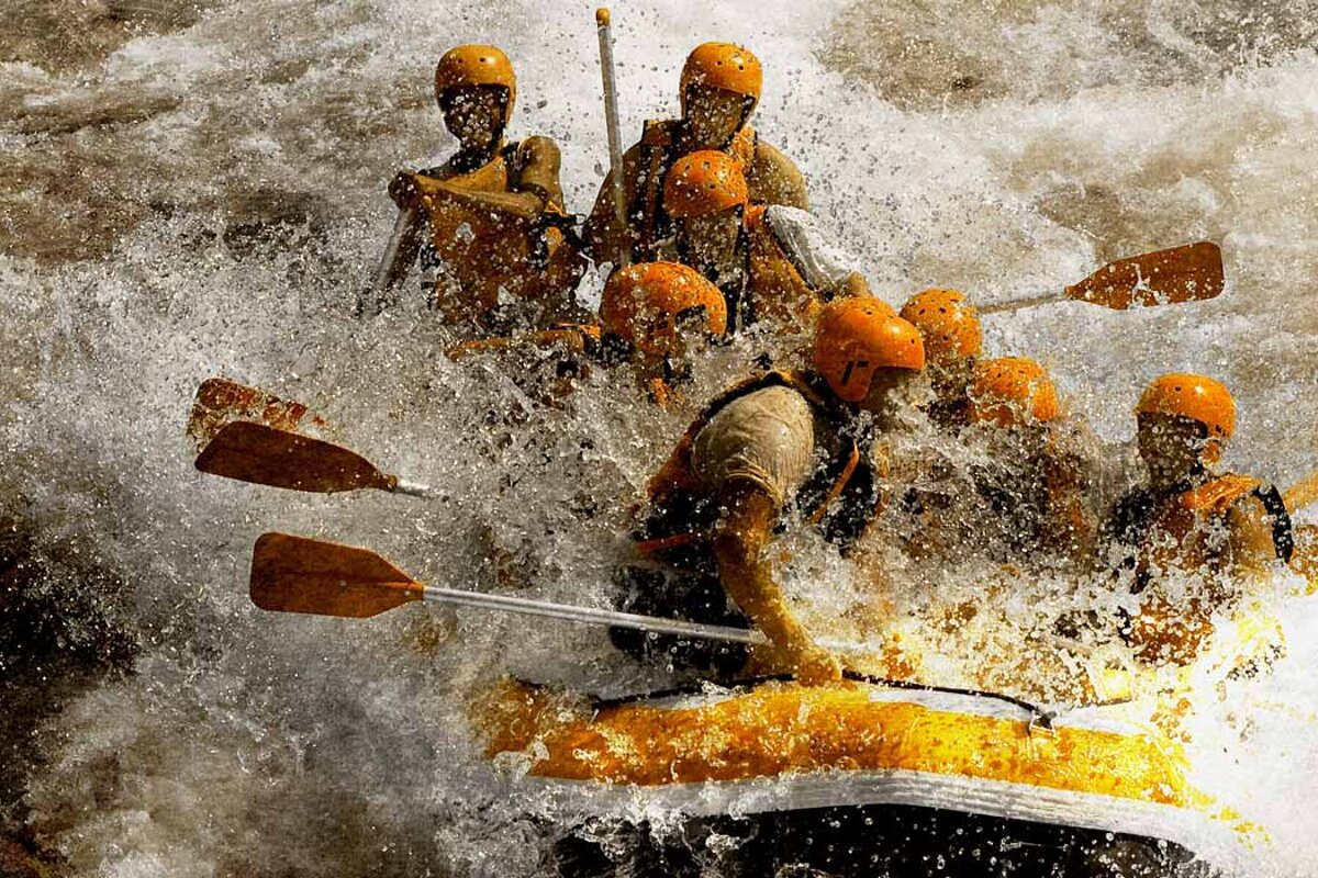 A group of people wearing orange helmets are rafting down a river