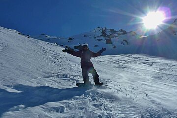 snowboarder with sunshine behind & wind blown snow
