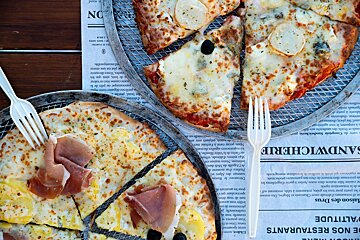 Three pizzas are sitting on a newspaper that says sandwicherie