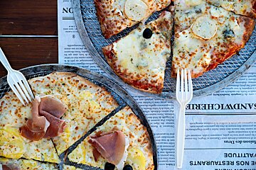 Three pizzas are sitting on a newspaper that says sandwicherie