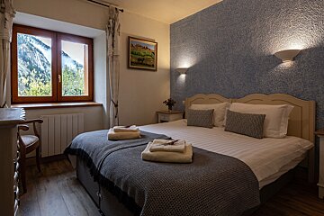 Cozy bedroom with a made bed, fresh towels, and a stunning mountain view from the window. Blue textured walls and warm lighting complete the inviting space.