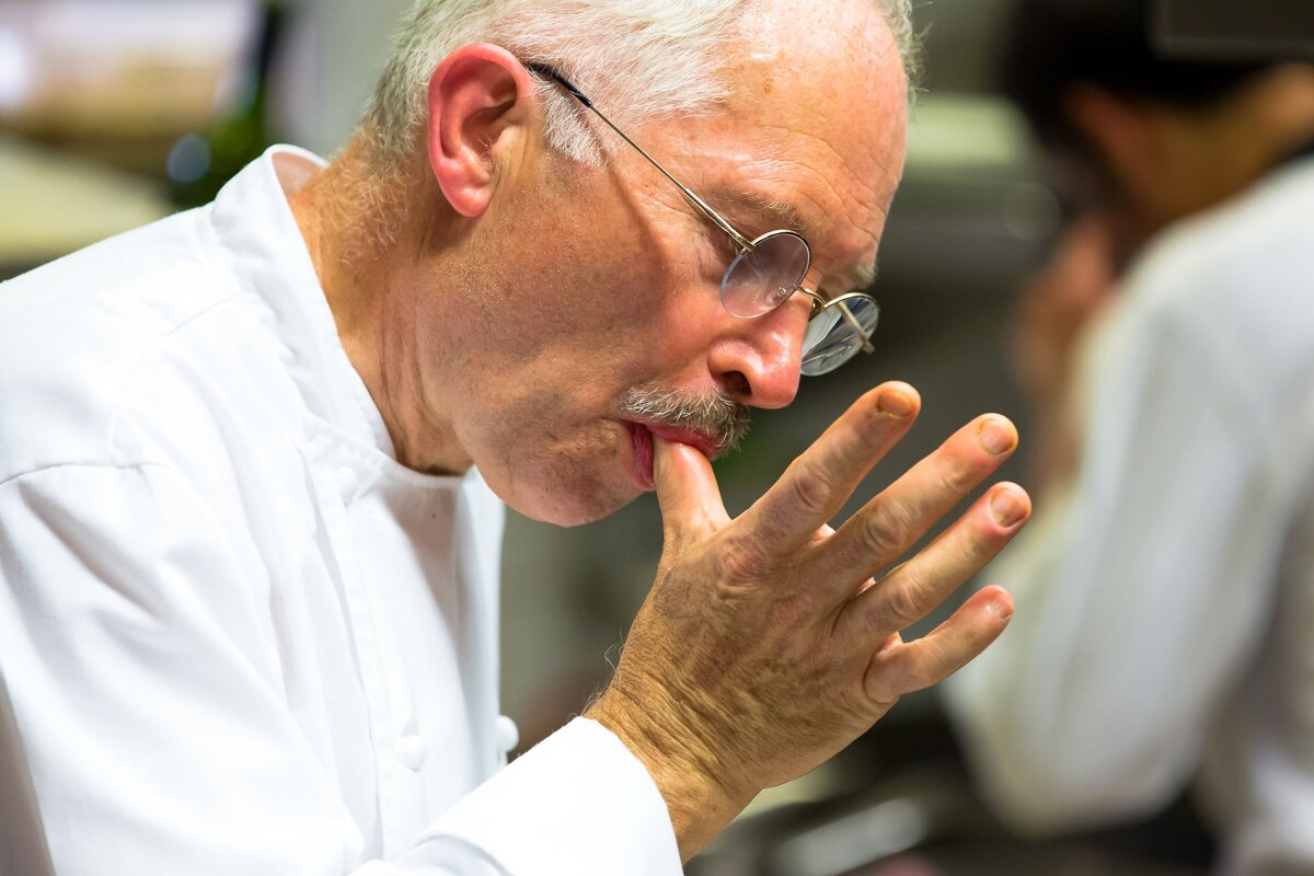 A man wearing glasses and a white shirt is licking his finger