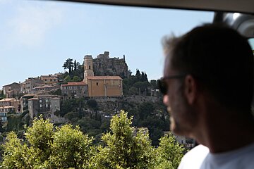 A man looking out a window at a castle on top of a hill