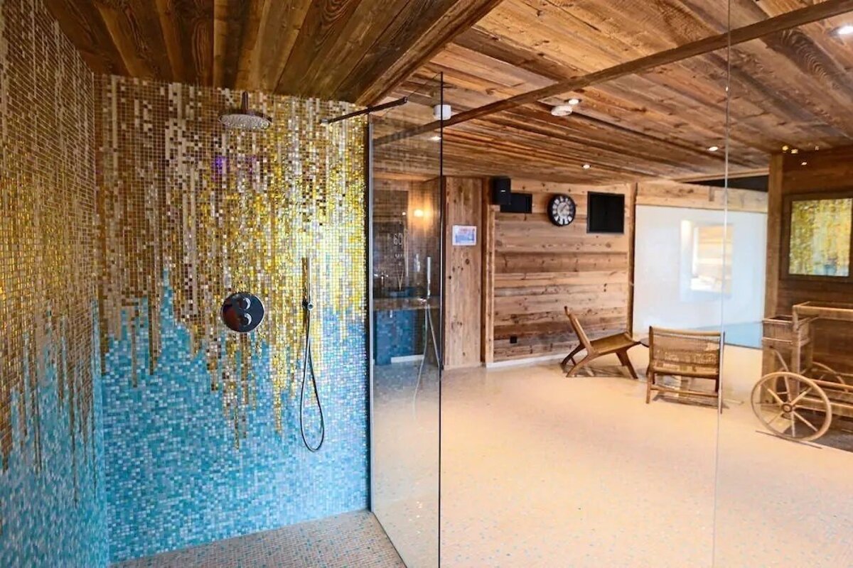 Modern spa shower with glass walls, gold and blue mosaic tile, and a wood-paneled ceiling.