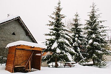 A wooden shed is covered in snow in front of a house