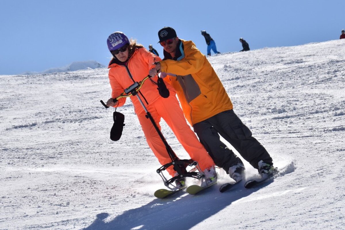 a man helping someone ski with handlebars