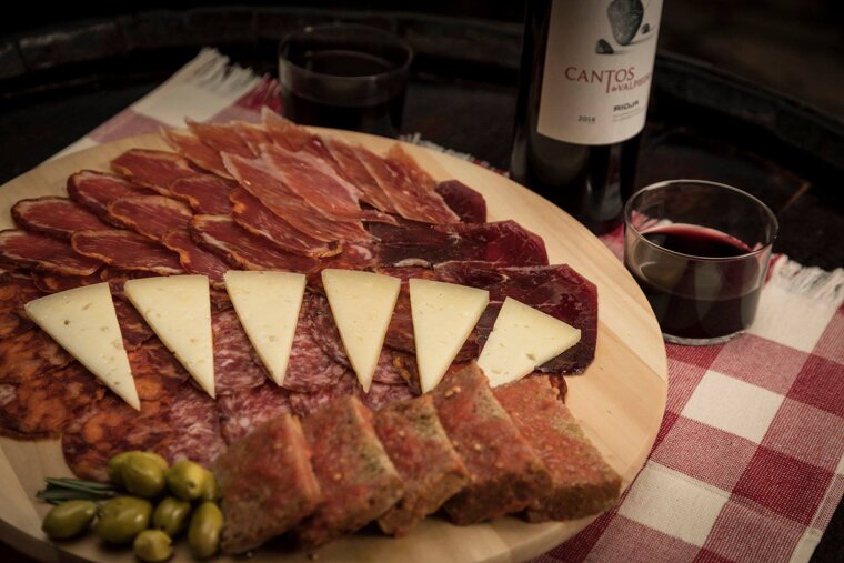 A bottle of cantos wine sits next to a plate of meat and cheese