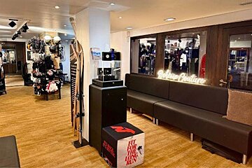 A stylish boutique interior with wooden floors, ski gear, clothing displays, a long dark sofa, and a 