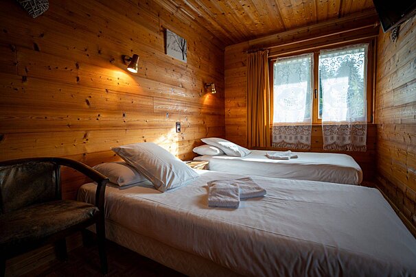 A wooden bedroom with two beds and a chair