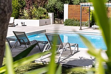 A swimming pool is surrounded by lawn chairs and a wooden fence