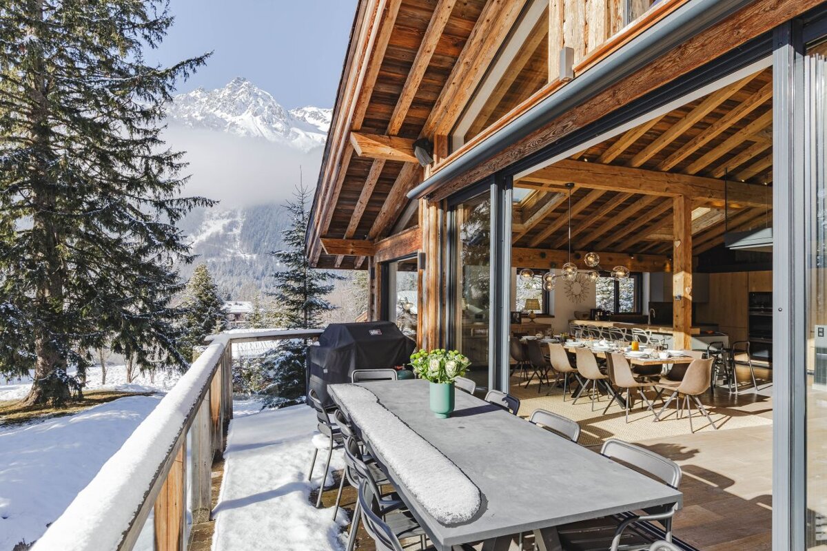 A large table and chairs on a balcony with mountains in the background