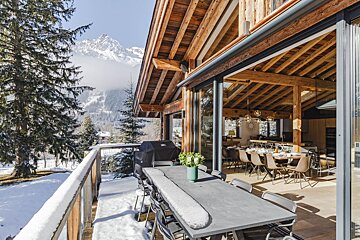 A large table and chairs on a balcony with mountains in the background
