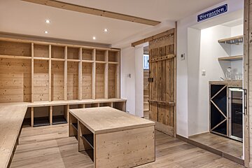 A rustic room with light wooden paneling, extensive shelving, a central table, a mini-bar, and a 