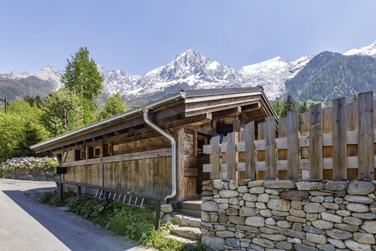 A wooden building with a stone wall and mountains in the background