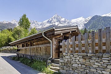A wooden building with a stone wall and mountains in the background