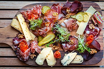 A delicious charcuterie and cheese board featuring sliced meats, various cheeses, pickles, walnuts, fresh greens, and a pat of butter.
