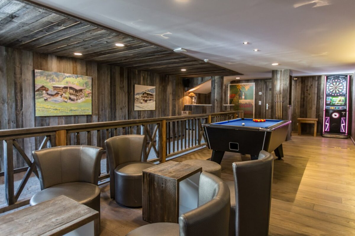 A pool table in a room with chairs and a dart board