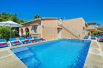 A swimming pool with blue chairs and umbrellas in front of a house