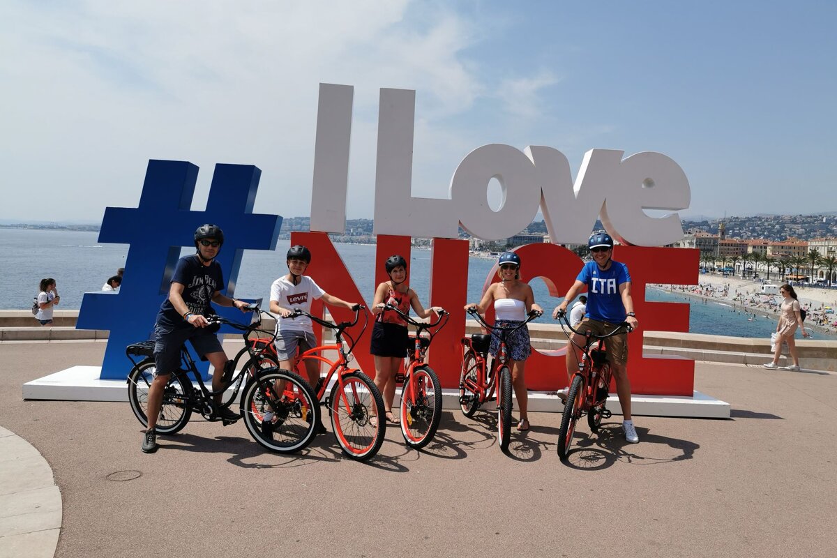 A group of people riding bikes in front of a sign that says i love nice