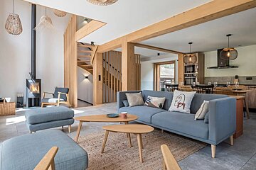 Modern open-plan living room featuring light wood accents, a blue sofa, wooden coffee tables, and a stylish staircase.