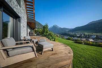 A wooden deck with chairs and ottomans with a view of mountains in the background