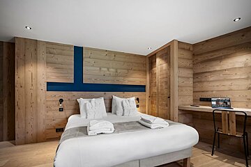 A bedroom with a bed and a desk with a laptop on it