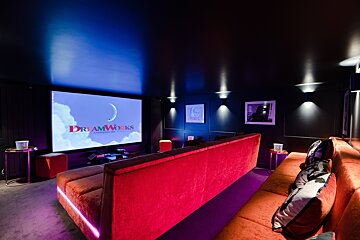 A stylish home cinema with a large screen displaying the DreamWorks logo, dark walls, red/orange seating, and vibrant accent lighting.