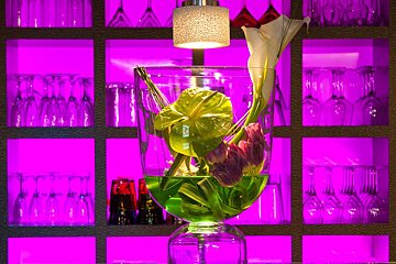 A vase filled with flowers sits in front of a shelf of wine glasses