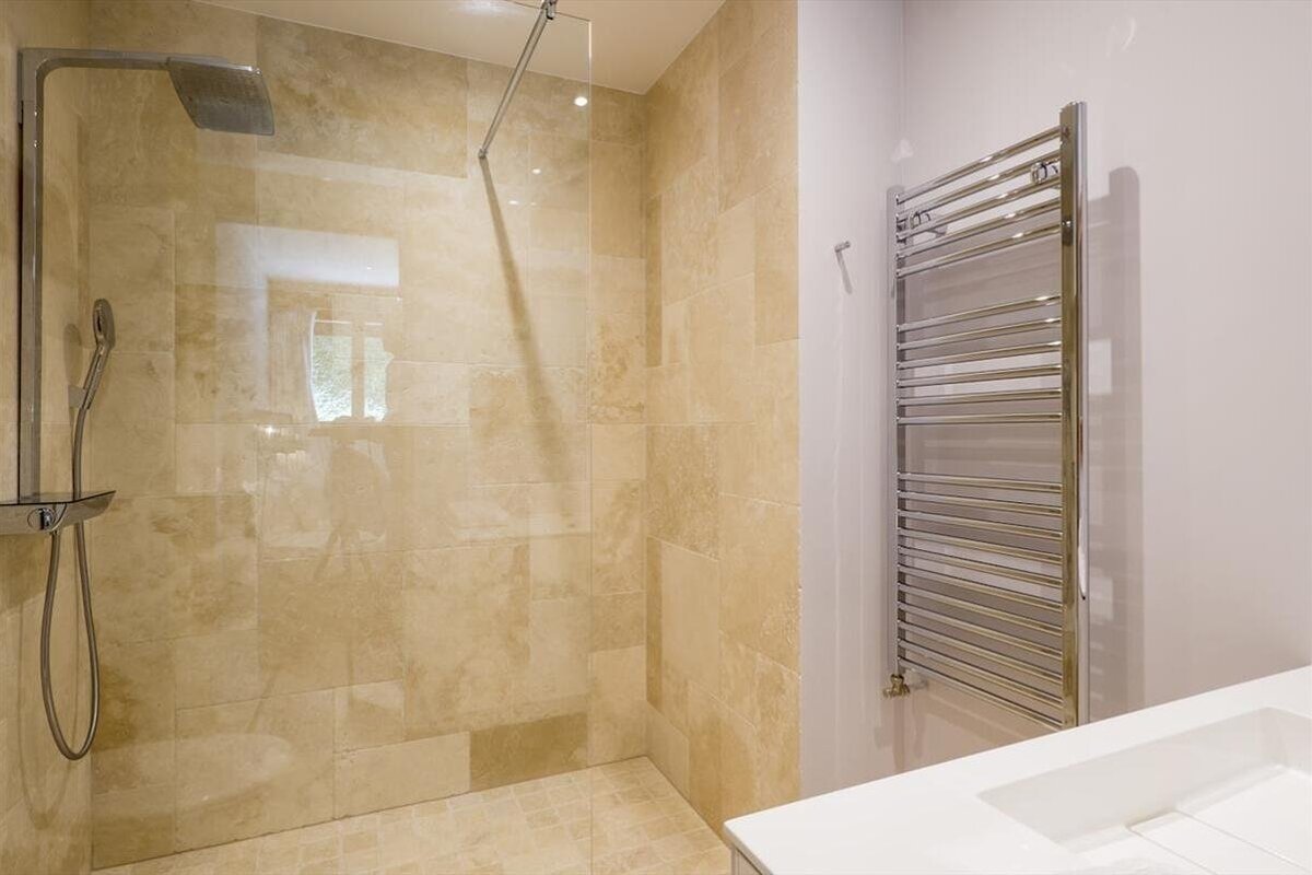 Modern bathroom with a beige tiled walk-in shower, glass screen, rain shower, and a chrome heated towel rail.