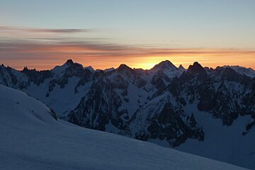 The sun is setting over a snowy mountain range