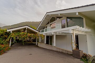 A large white house with a balcony and mountains in the background