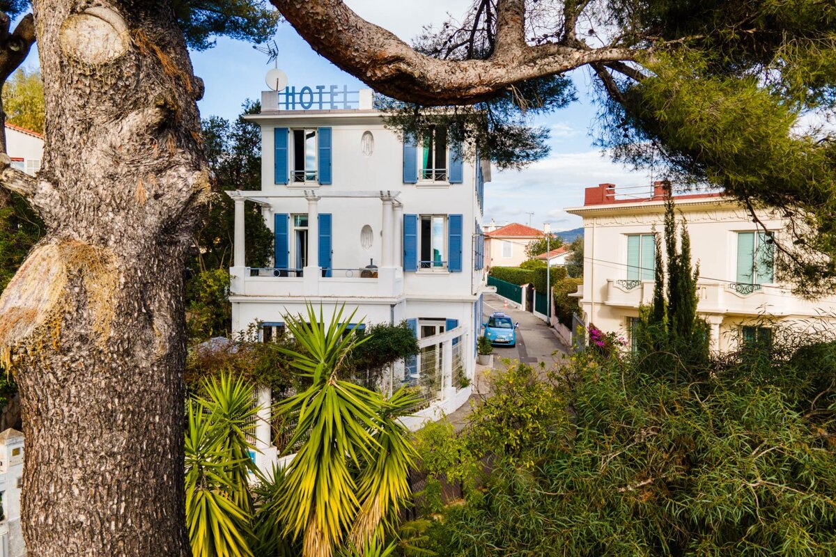 A white building with blue shutters has the word hotel on the top