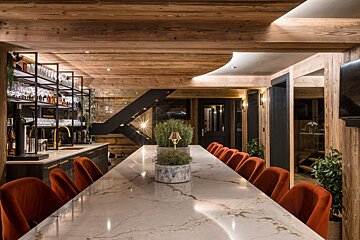 A long marble table with red chairs in a room