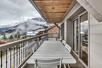 A balcony with a table and chairs and mountains in the background