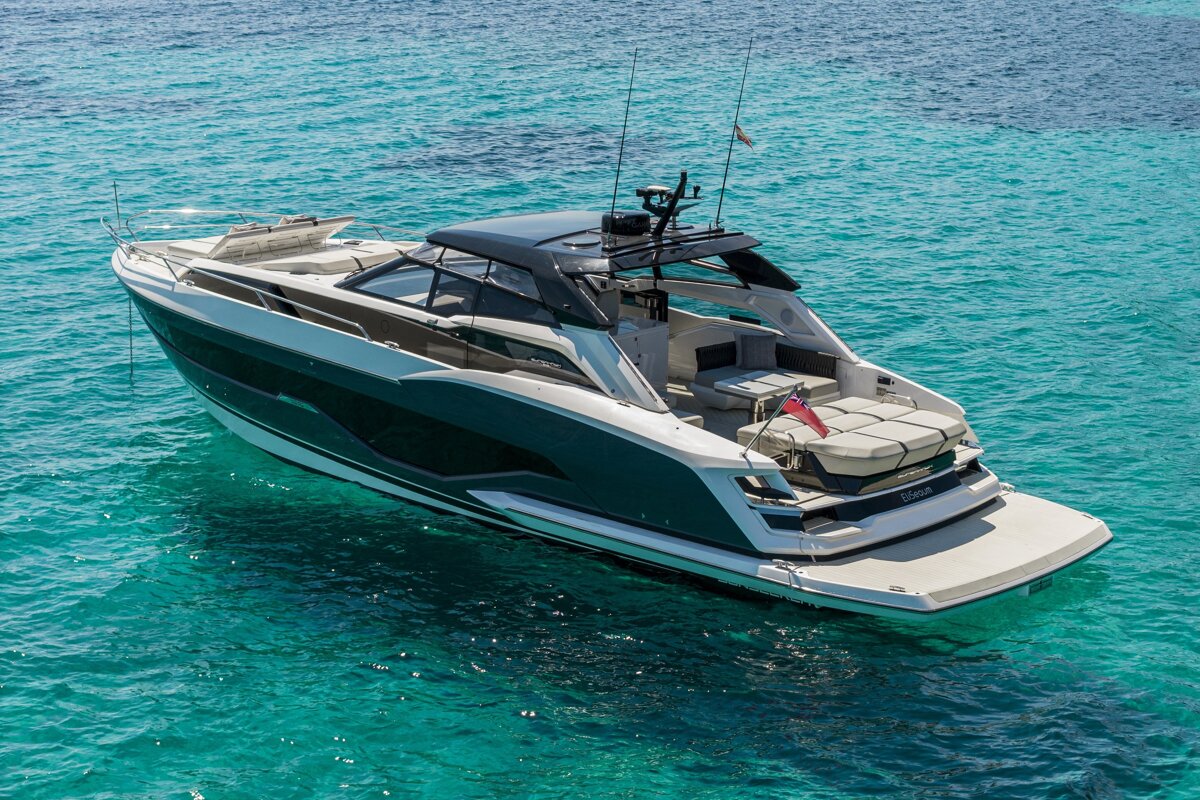 A sleek dark green and white luxury yacht floats in dazzling turquoise water on a sunny day.