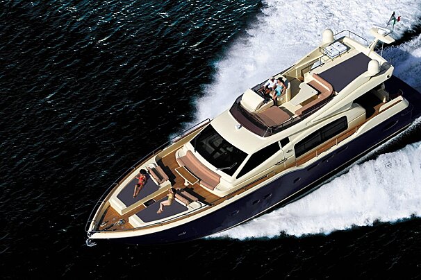 A luxurious blue and cream yacht speeds through dark water, creating a white wake. People sunbathe on the bow and relax on the flybridge.