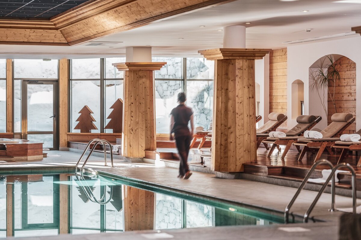 A woman is walking towards a large indoor swimming pool