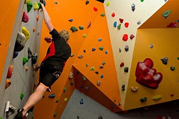 A man climbs a climbing wall with a lego heart in the background
