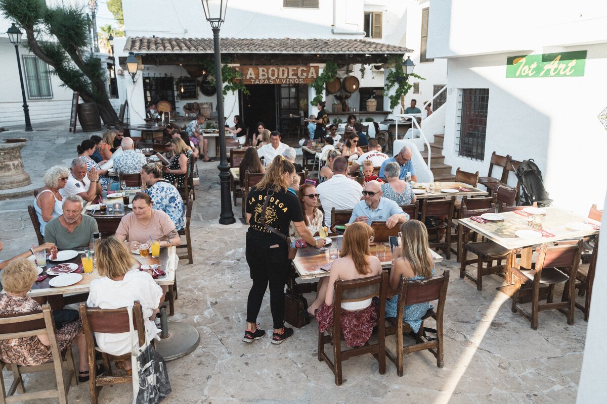 A large group of people are sitting at tables in front of a bodega restaurant