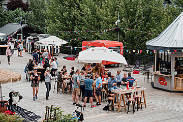 A group of people are gathered around tables and umbrellas on a deck