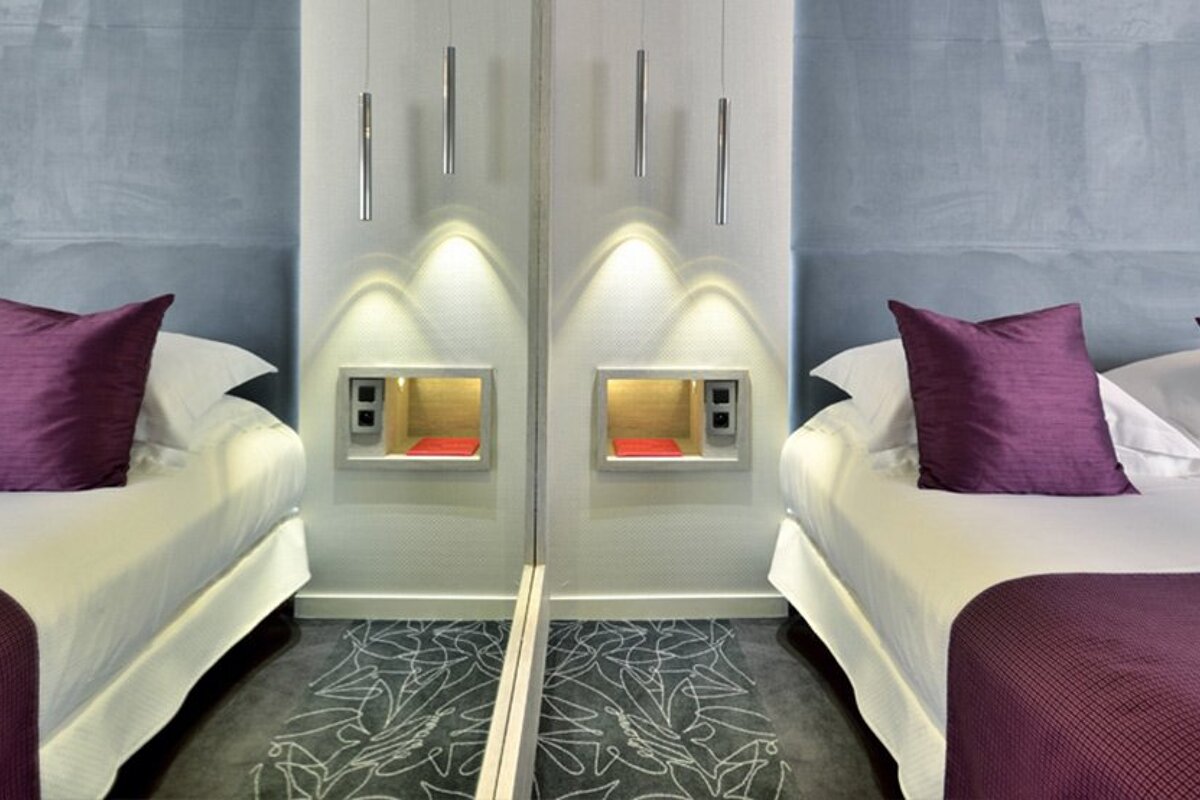 Two beds with purple pillows in front of a mirror